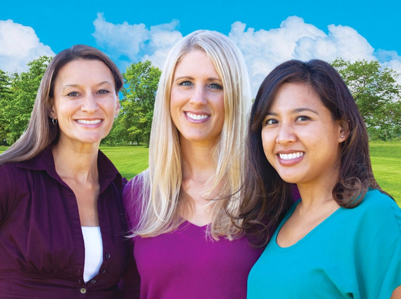Three women smiling in outdoor setting.